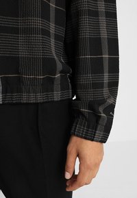 Camicia a quadri nera con un motivo testurizzato, dalla vestibilità comoda e polsini elasticizzati. Il tessuto è morbido, messo in risalto da linee grigie a contrasto.