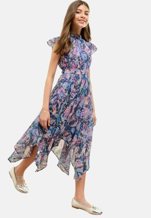 Multikleurige bloemenjurk met ruchemouwen, asymmetrische zoom en een taille die is aangesnoerd. Gecombineerd met zilveren balletschoenen.