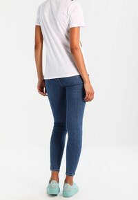 Hvid kortærmet t-shirt, blå skinny jeans og lyseblå sneakers; set fra ryggen, som viser en tætsiddende silhuet og glatte teksturer.