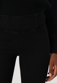 Pantalones negros de tiro alto con una textura suave y un leve estiramiento. Presentan una parte delantera plana y sin hardware visible ni bolsillos.