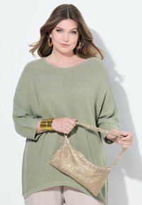 Maglione verde a maglia morbido e testurizzato con scollo a barca, abbinato a una borsa a tracolla in oro con una finitura metallica lucida.