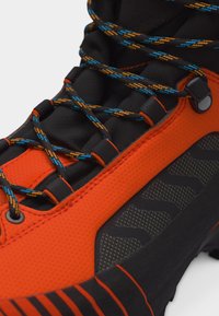 Κοντινή λήψη πορτοκαλί και μαύρου παπουτσιού πεζοπορίας με κορδόνια σε μοτίβο μπλε και πορτοκαλί και λεπτομέρεια τραχιάς σόλας.