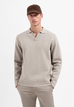 Hellbeige Langarmpoloshirt mit V-Ausschnitt und weicher Textur. Kombiniert mit beigen Hosen und einer braunen Mütze. Einfaches und modernes Design.