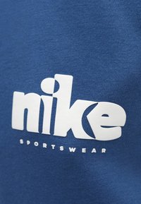 Modrá mikina s veľkým bielym logom "nike" a nápisom "SPORTSWEAR", vyrobená z mäkkého, textúrovaného bavlneného materiálu.