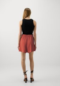 Mustat hihattomat tee-paidat yhdistettynä ruosteenvärisiin shortseihin, joissa on joustava vyötärö. Shortseissa on teksturoitu kangas ja kaareva helma.