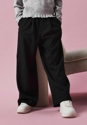 Pantalones de pierna ancha a rayas negras combinados con un suéter gris que cuenta con un borde de encaje blanco, complementados por zapatillas blancas.