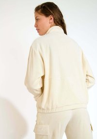 Giacca zip in corduroy crema con colletto alto e tasche laterali; tessuto texturizzato e design rilassato.