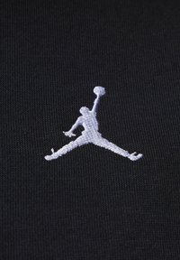 Sort stof med et hvidt broderet Jumpman-logo, der viser en figur i luften, som holder en basketball. Tekstureret, sporty design.