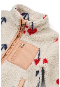 Flis jakna v kremni barvi z barvnimi vzorci src in puščic. Ima tan barvni žep z zadrgo in visok ovratnik za toploto.