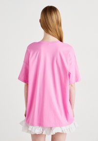 Růžové bavlněné tričko s krátkými rukávy a volným střihem, s kulatým výstřihem. Nosené přes bílou sukně s volánky.