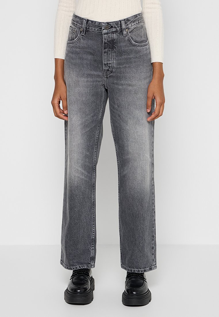 Jeans grigi alti in vita e a gamba larga con una finitura scolorita, cinque tasche, chiusura con bottone metallico e cerniera, abbinati a scarpe con tacco alti nere.