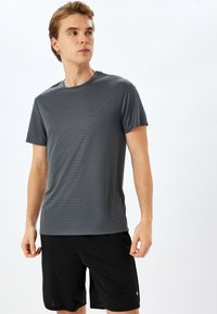 Grijs T-shirt met korte mouwen en een gestructureerd oppervlak, gecombineerd met zwarte shorts. Het shirt heeft een ronde halslijn en een slim fit ontwerp.