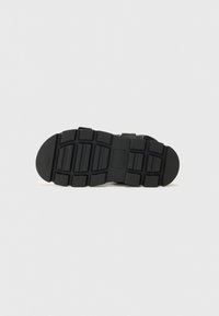 Black rubber shoe sole with a textured, multi-directional tread pattern and circular heel. Flat design suitable for various surfaces.