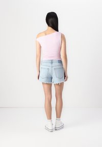 Rosa ensidig topp og lyseblå ripped denim shorts. Modellen har på seg hvite høyhælte joggesko, og står foran en ensfarget bakgrunn.