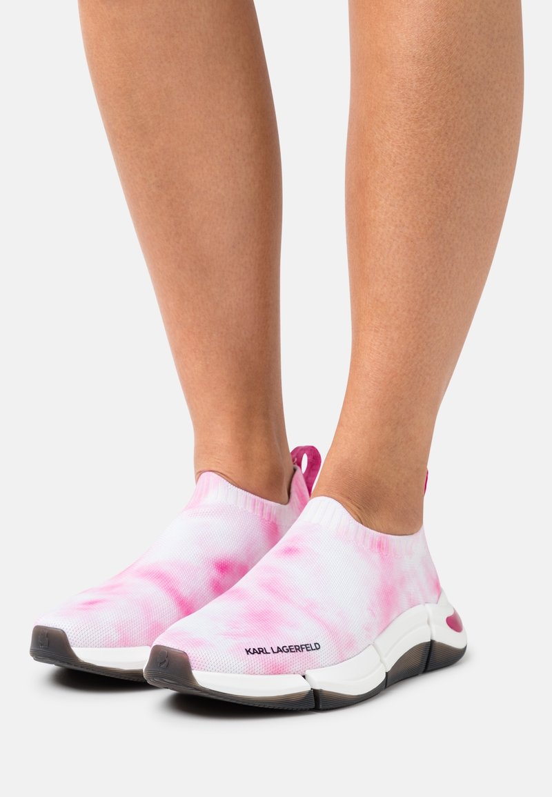 Pieds portant des baskets slip-on tie-dye roses et blanches avec semelles noires et blanches et marquage "KARL LAGERFELD" sur le côté.