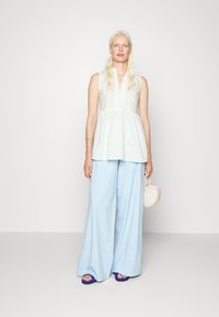 Top branco sem mangas com uma lista de botões, combinado com calças largas azul claro. Os acessórios incluem uma pequena bolsa branca e sandálias azuis.