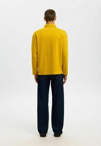 Gelbes Langarmhemd mit Kragen, aus strukturiertem Stoff, kombiniert mit lockeren, dunkelblauen Jeans mit Gesäßtaschen und gerader Passform.