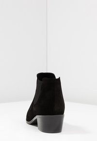 Schwarze Wildleder-Stiefelette mit niedrigem Blockabsatz, elastischen Seitenpaneelen und einer glatten, abgerundeten Spitze. Einfaches, elegantes Design ohne sichtbare Beschläge.