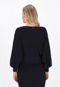 Granatowy, krótki sweter z szerokimi rękawami, teksturowany materiał dzianinowy oraz mały złoty akcent z tyłu przy dekolcie.