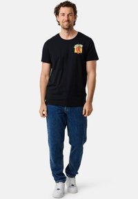 Sort bomulds t-shirt med et farverigt grafisk design på brystet. Parret med blå denim jeans og hvide sneaks.