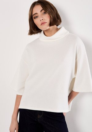 Witte wafelstructuur top met een hoge hals, korte mouwen en een losse pasvorm, gecombineerd met donker denim jeans.