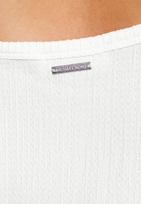 Top bianco in tessuto texturizzato con un design a righe sottili, con un'etichetta del marchio "MICHAEL KORS" in argento cucita vicino al collo.