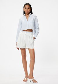 Lyseblå stribet cropped skjorte med lange ærmer og brystlomme, parret med hvide højtaljede shorts med plisseringer og elastisk talje.