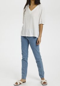 Hvid v-hals bluse med korte puffærmer, båret med lys blå skinny jeans og beige slidesandaler med et snoet stropdesign.