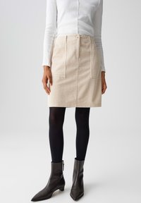 Beige corduroy rok met twee voorzakken, hoge taille en knoopsluiting, gecombineerd met zwarte panty’s en enkellaarsjes met een hak.