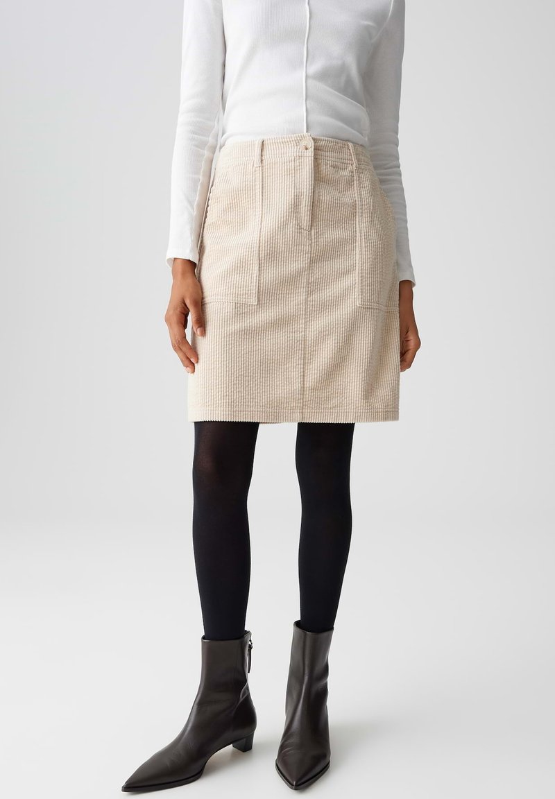 Beige corduroy rok met twee voorzakken, hoge taille en knoopsluiting, gecombineerd met zwarte panty’s en enkellaarsjes met een hak.