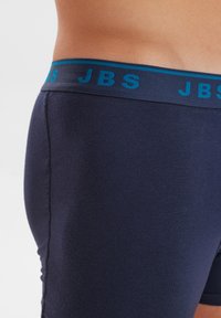 Bóxer azul marino de tela suave, con una cinturilla elástica turquesa contrastante que lleva el logo "JBS".