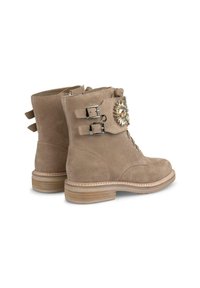 Stivaletti alla caviglia in suede beige con due fibbie argentate e un dettaglio decorativo in gemma. Presentano una punta rotonda e un tacco impilato in legno chiaro.