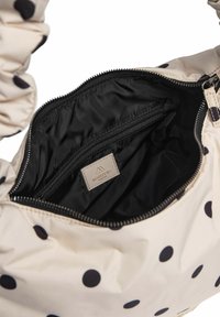 Beige håndtaske med polka prikker, sammensunkne tekstilhanke, en sort lynlås, og et indre rum med en lille lynlås-lomme og logo mærke.