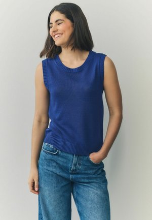 Débardeur en tricot sans manches bleu avec un col rond et un ourlet côtelé, associé à un pantalon en jean bleu clair. Texture lisse et design ajusté.