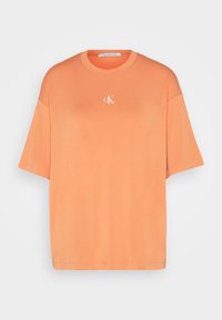 Camiseta de algodón naranja con mangas cortas, un cuello redondo y un pequeño logo blanco "ck" centrado en el pecho. Textura suave y ajuste relajado.