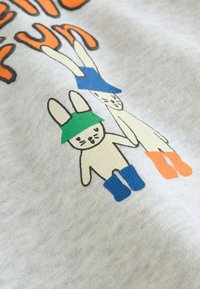 Dva kreslené králiky držia sa za ruky na látke, jeden s zeleným klobúkom a modrými čižmami, druhý s modrým klobúkom a oranžovými čižmami.