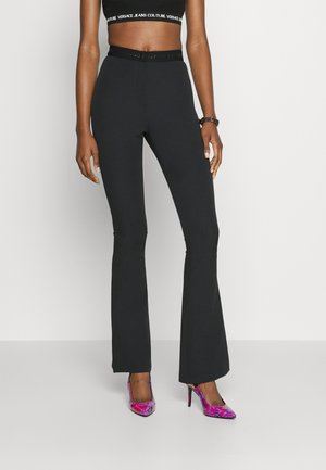 Pantalones de campana negros con un alto cinturón que presenta un acento brillante. Combinados con zapatos de tacón alto de patrón rosa y morado.