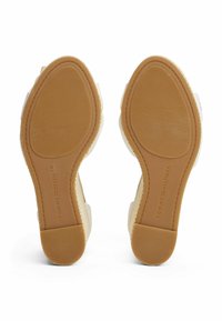 Las sandalias de plataforma blancas cuentan con una suela de goma texturizada en color marrón. La marca destacada en la suela dice "TOMMY HILFIGER". Material superior suave.