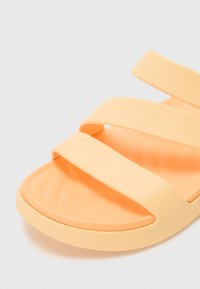 Orange slip-on sandal with three wide straps. Made of smooth rubber material. Slightly rounded toe and textured insole for comfort.