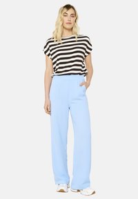 Camiseta de rayas en blanco y negro con un corte holgado, combinada con pantalones de pierna ancha de color azul claro. Zapatillas blancas completan el atuendo.