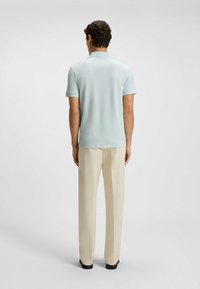 Light blue polo shirt with short sleeves and a collar, paired with cream-colored trousers, viewed from the back. Smooth texture and simple design.