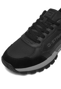 Melnas sporta kurpes ar teksturēta tīklojuma un gluda zamša apvienojumu. Kurpju auklu dizains ar mīkstinātu zoli un izcelto zīmola uzrakstu.