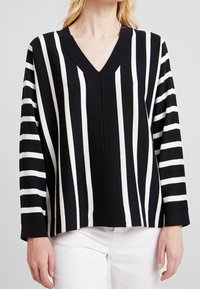 Black and white striped v-neck sweater with long sleeves, featuring alternating wide and narrow stripes and a relaxed silhouette.