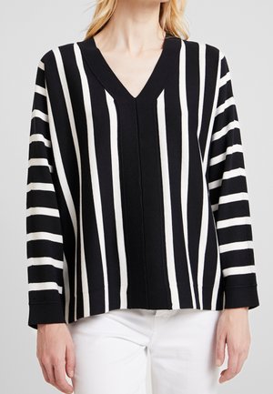 Pull à col en V noir et blanc rayé avec des manches longues, affichant des rayures larges et étroites alternées et une silhouette décontractée.