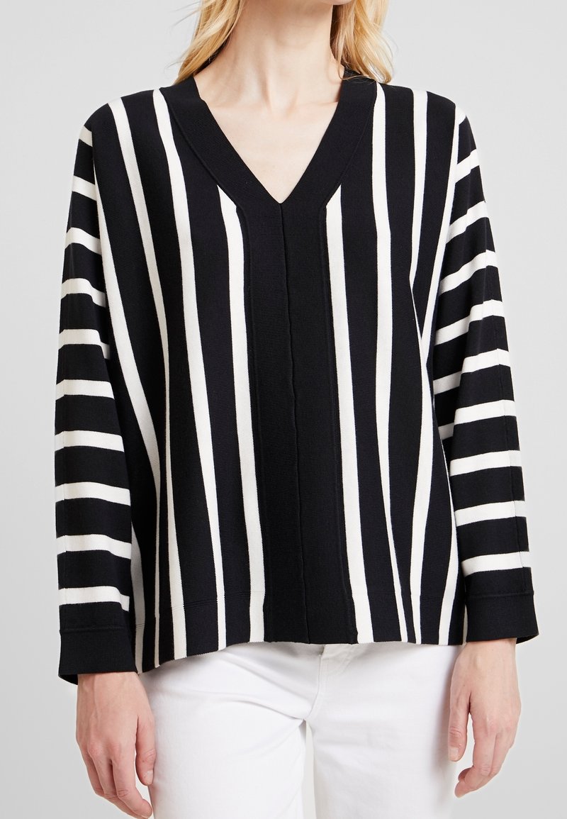 Black and white striped v-neck sweater with long sleeves, featuring alternating wide and narrow stripes and a relaxed silhouette.