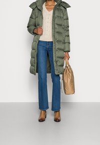 Olivengrøn puffjakke med hætte, beige striktrøje, blå lige ben jeans, brune ankelstøvler og en lysebrun snorepose.