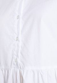 Blusa bianca in cotone con fronte abbottonato, tessuto texturizzato e dettaglio arricciato all'orlo. Stile classico con bottoni standard.