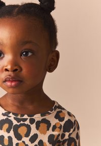 Child wearing a ribbed, beige top with black and brown leopard print. The fabric has a textured look, and the neckline is rounded.