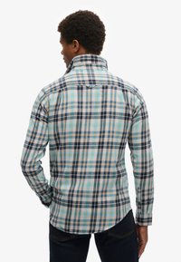 Camisa de cuadro para hombre con tonos azules, marinos y beige, con cuello tipo polo y mangas largas. Fabricada en algodón con una textura suave.