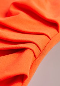 Un tissu orange vif présente une texture lisse avec plusieurs plis, mettant en valeur un design extensible et des bords nets.